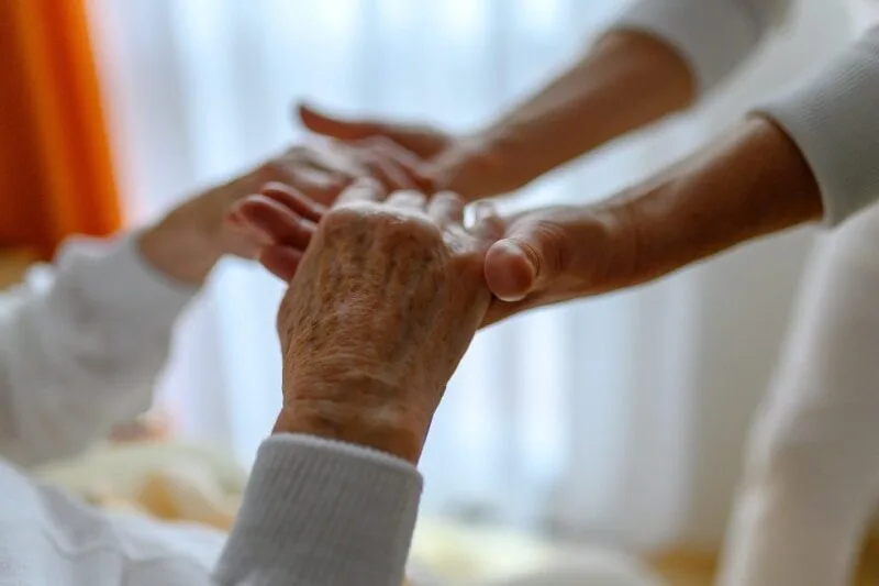 Pflegekraft hält die Hände eines älteren Menschen